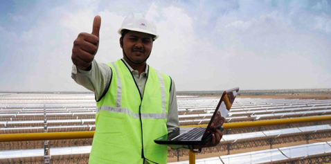A man next to a solar power plant, doing a thumbs up sign. Photo.