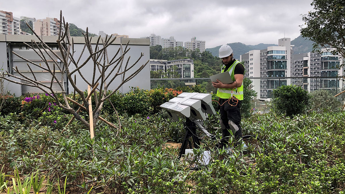 A man installing equipment on a city roof with many plants. Photo.