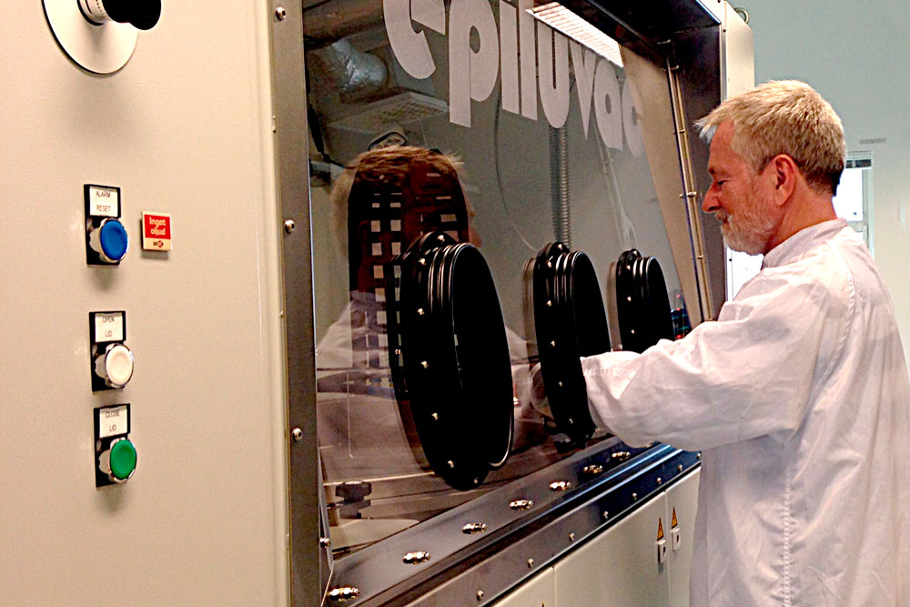 A man in a white coat stands with his hands in a large machine.