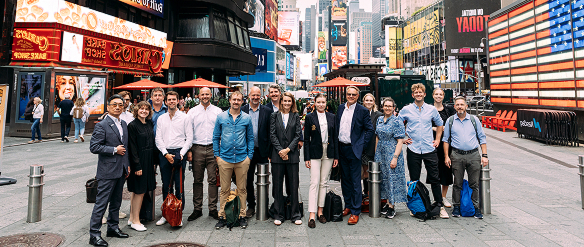 A group of about 15 people, part of the 'Skyline delegation', stand for a photo in Times Square, New York City, surrounded by large digital billboards.